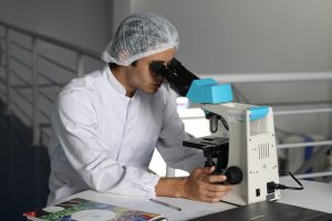 A microbiologist studying microorganisms through microscope